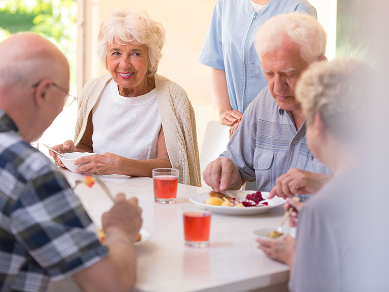 Vier Senioren sitzen gemeinsam an einem hellen Esstisch und unterhalten sich während der Mahlzeit.