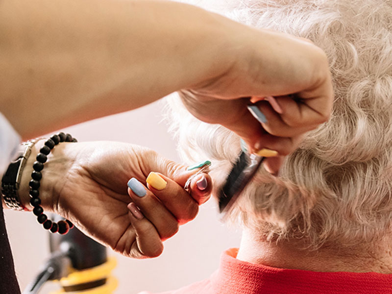 Hände einer Friseurin beim Haareschneiden bei einer älteren Dame.