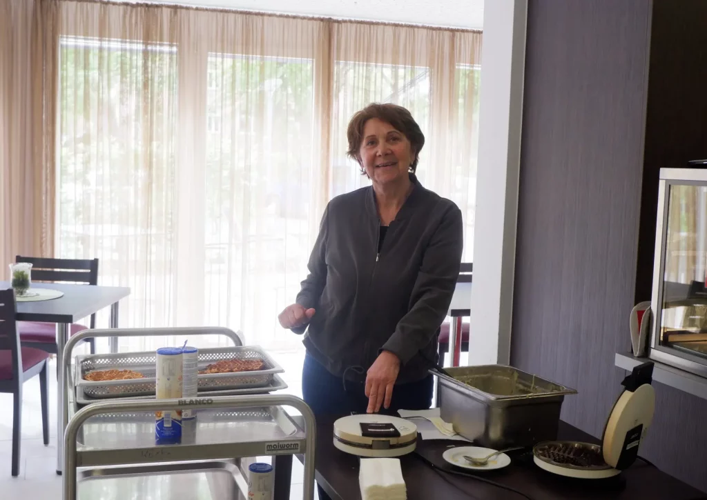 Eine Frau backt Waffeln und lächelt in die Kamera.