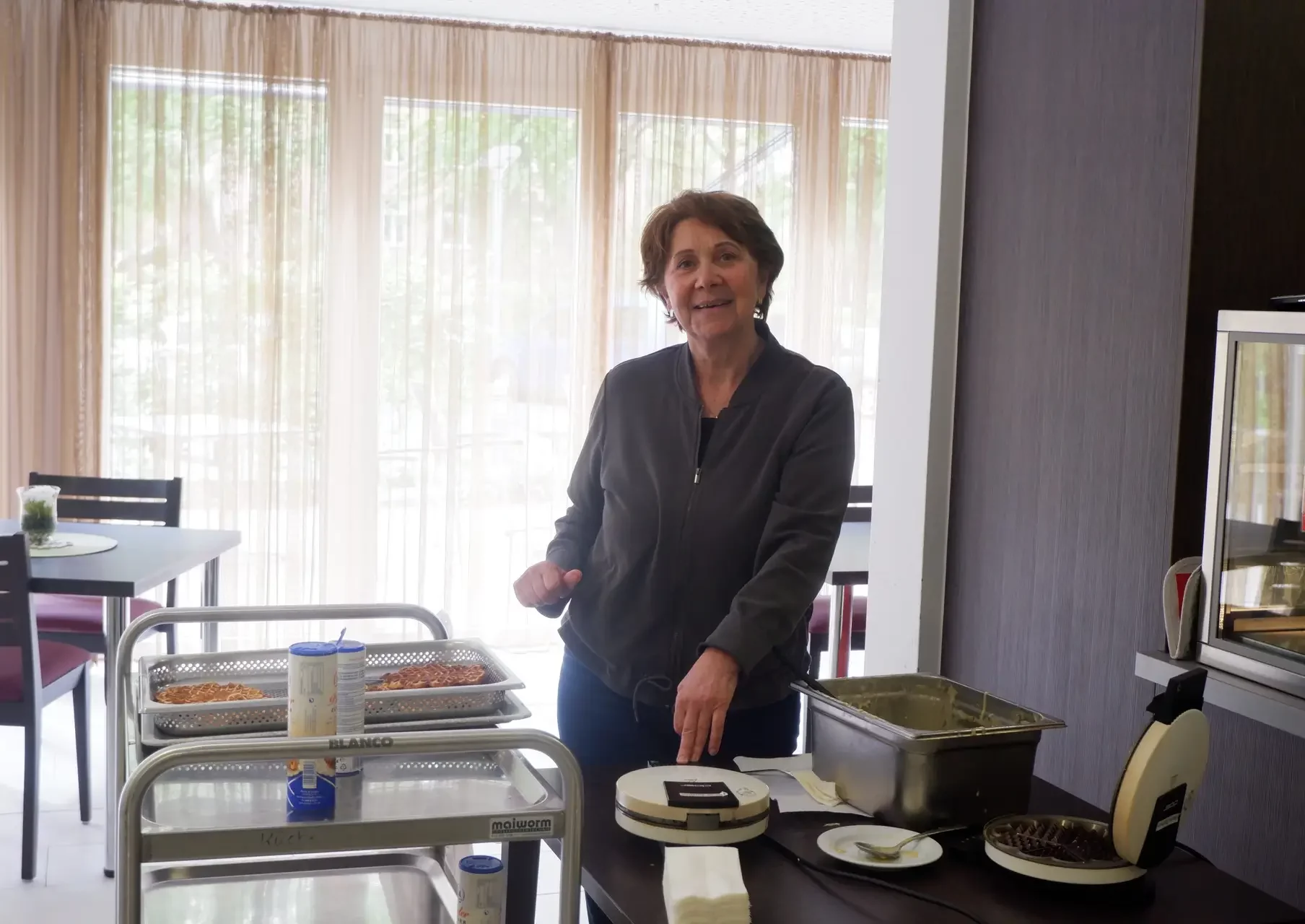 Eine Frau backt Waffeln und lächelt in die Kamera.
