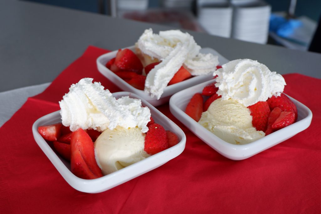 Drei Schälchen mit frischen Erdbeeren, Sahne und Vanilleeis stehen auf einem Tisch.