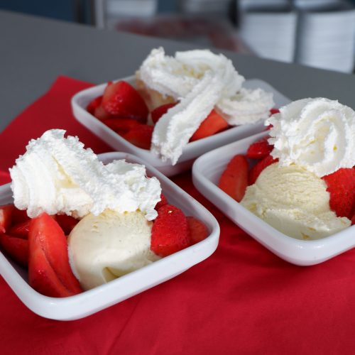 Drei Schälchen mit frischen Erdbeeren, Sahne und Vanilleeis stehen auf einem Tisch.