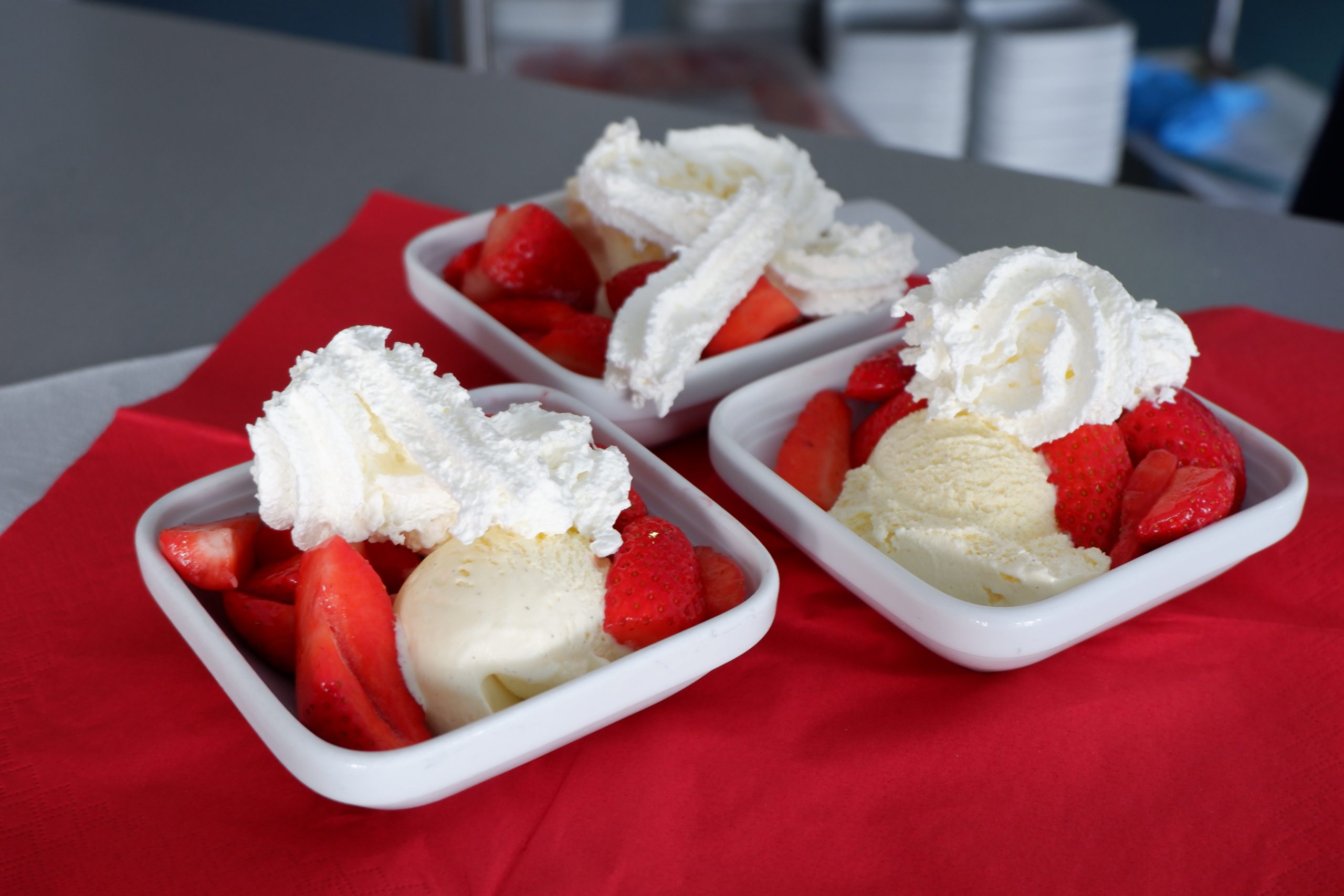 Drei Schälchen mit frischen Erdbeeren, Sahne und Vanilleeis stehen auf einem Tisch.